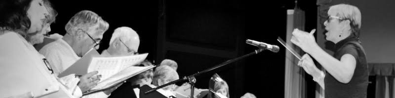Lorilee Bajema conducting a community choir in performance, in black and white