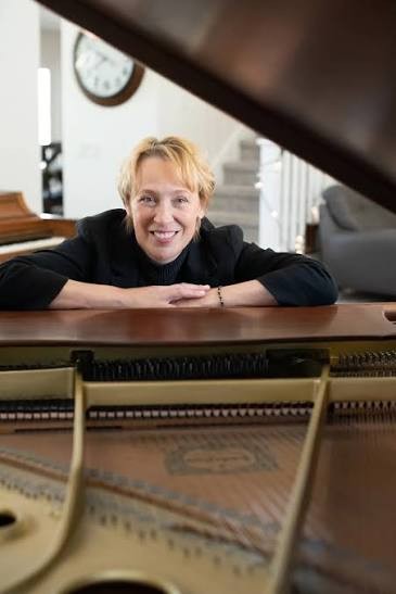 Lorilee Bajema smiling over the open lid of her grand piano, strings and soundboard in the foreground