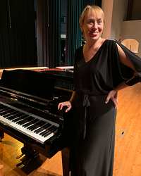Lorilee Bajema smiling, standing beside a grand piano on a stage