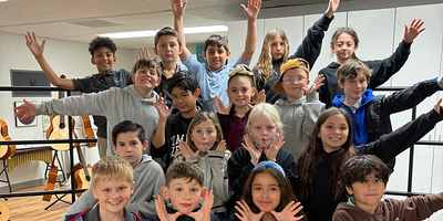 A crowd of school-age choir students with their arms stretched wide, grinning at the camera