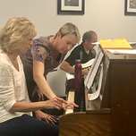 Lorilee leaning in to help a student at the piano